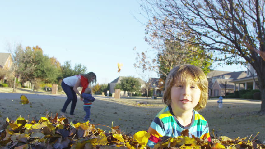 Boy scoops up leaves and throws them into the camera lens