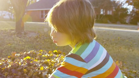 Close up of a boy as he rakes leaves with a sun flare