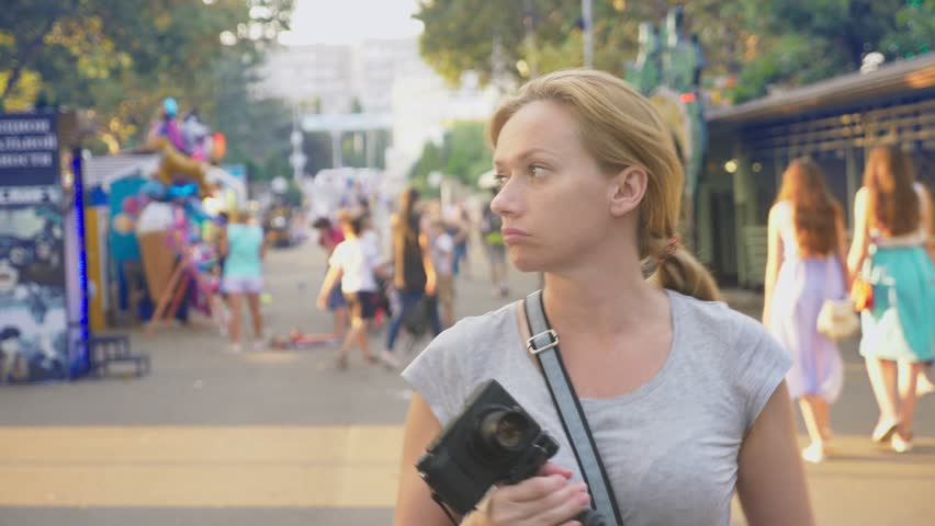 a professional photographer, takes pictures in an amusement park, a woman presses a button of a gadget among a flowering garden. 4k, slow motion, steadicam shooting