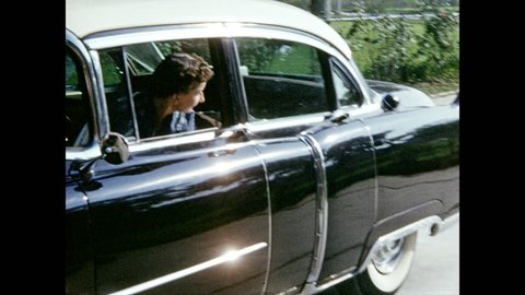 1950s: Woman backs car out of driveway, looks out window, waves.
