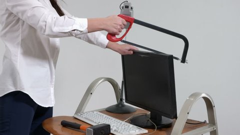 Angry office worker destroying desktop computer with hacksaw and sledgehammer