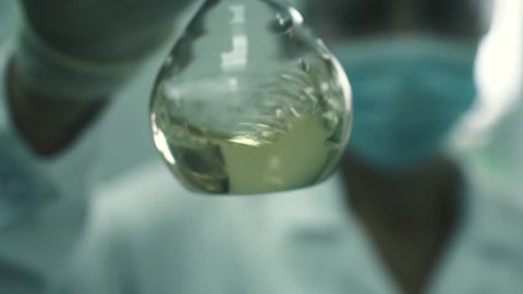Girl lab assistant stirs the liquid in a flask