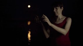 A young woman makes a video call on the background of a red plenilune, a rare astronomical phenomenon. The girl smiles and waves her hand. The orange moon is reflected in the river.