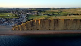 Drone tracks sideways along the cliff and beach in West Bay in the Dorset countryside. Shot during sunset