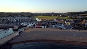 Drone flies back from West Bay beach with Bridport and the Dorset countryside in the background. Shot at sunset.