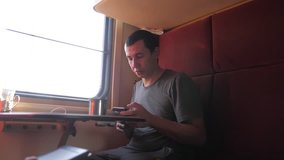 man is sitting on the train Railway carriage holding a smartphone and drinking coffee and tea. slow motion video. man writes messages in lifestyle the smartphone in the train social media. man with