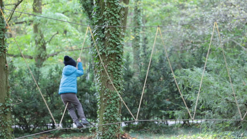 Cute child, boy, climbing in a rope playground structure, springtime