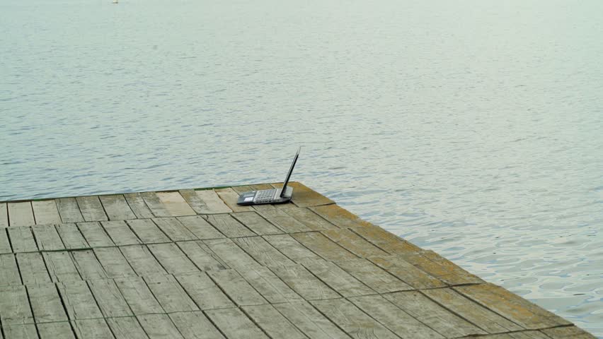 Young man working on laptop while sitting ?n old pier