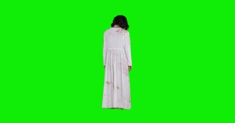 Creepy zombie woman with wounded face and white gown standing in the studio, shot in 4k resolution with green screen background
