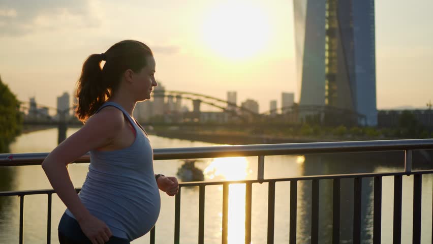 Active pregnant woman running across the bridge with a beautiful view of the city of Frankfurt in Germany