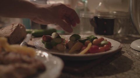 Hands grabbing vegetables and putting them on a plate with cooked chicken in 4k.