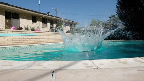 Young fit Caucasian man runs off diving board and jumps into a swimming pool in a backyard. Man in swimming trunks jumps into an outdoor swimming pool. Jumping into backyard pool making a splash.