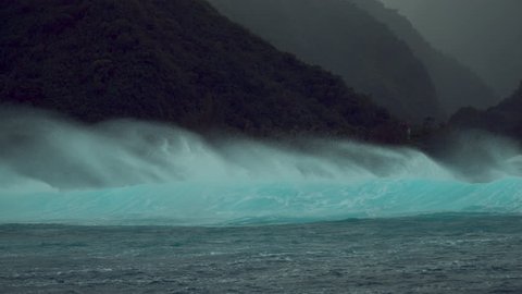 SLOW MOTION: Large turquoise breaking ocean wave approaches a tropical island in the Pacific covered with lush green rainforest. Bad weather and raging waves closing in on a remote exotic island.