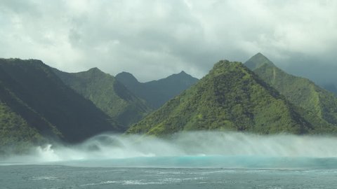 SLOW MOTION: Beautiful mist rolls behind a turquoise swell approaching exotic island before a violent rainstorm. Cinematic shot of dark clouds gathering above mountains looking over the powerful ocean