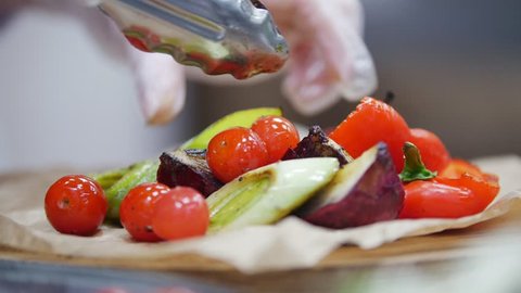 Unknown chef adds cherry tomatoes to cooked vegetables, in the frame of the chef's hand: film stockowy