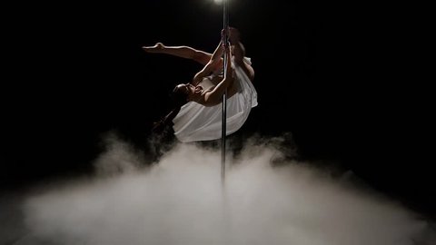 Stripper doing pole dance dark studio . Black smoke background. Slow motion