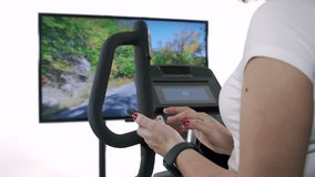 Woman checking workout on smart phone while exercising on elliptical trainer