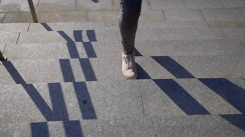 Close-up of woman legs in pink shoes and jeans climb the stone stairs up on a Sunny day