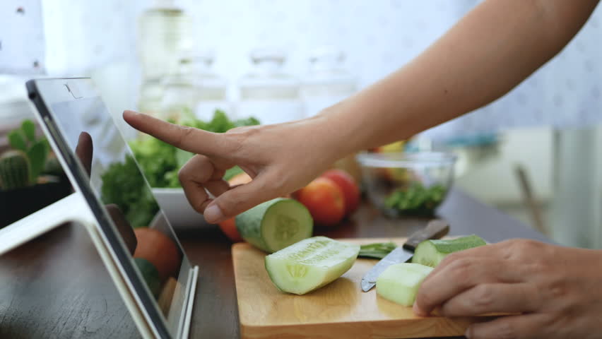 4K. woman use finger slide on tablet screen and peel a cucumber, prepare ingredients for cooking follow cooking online video clip on website via tablet. cooking content on internet technology Royalty-Free Stock Footage #1015736479