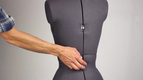 hand of tailor like a plastic surgeon gently change waist size and width of the back on a female sewing mannequin, tightening the adjusting screw, gray background