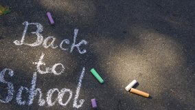Back to school background. Words written by child outdoor on sunny  grey asphalt texture with white chalk. Many other colorful chalks laying around. Real time 4 k video footage.