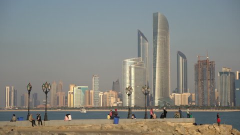 Abu Dhabi, United Arab Emirates - April, 2016: Tourists relaxing on the seafront, across the skyscrapers of Abu Dhabi