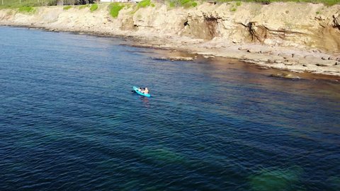 An aerial shot of a family paddling a kayak along the ocean coast of Cape Breton Nova Scotia Canada