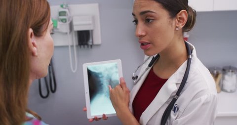 Portrait of young doctor using tablet to review x ray of female patients neck. Close up of attractive latina doctor and senior patient looking at x-ray of spine and cranium