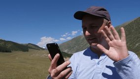 Smiling man in cap waving and having video chat on phone in Tian Shan mountains, Kyrgyzstan