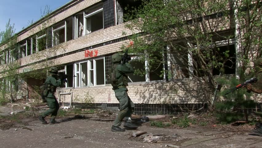 Airsoft players on background of destroyed house. Sports team game using a copy of a firearm. People in military uniforms with weapons at the exercises.