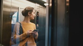 Young happy woman riding elevator with glass wall up, door opens and she walks out smiling using smartphone shopping app - Powered by Shutterstock - Get 15% off with code: PIKWIZARD15