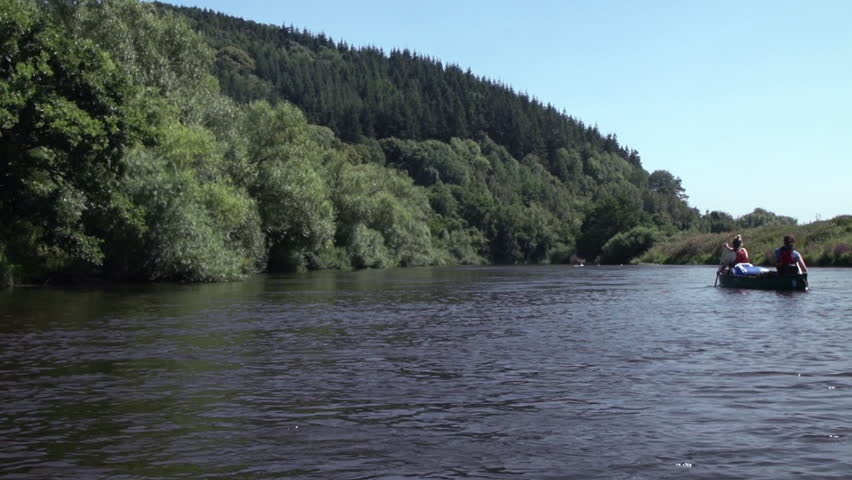 Two canoeists paddle off in to the distance down a river in the English countryside
