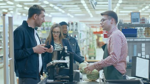 At the Supermarket: Checkout Counter Customer Pays with Smartphone for His Items. Big Shopping Mall with Friendly Cashier, Small Lines and Modern Wireless Paying Terminal System. Shot on RED EPIC-W 8K
