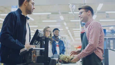 At the Supermarket: Checkout Counter Happy Customer Chats with Friendly Cashier who Scans Fresh Groceries and Fruits. Modern Shopping Mall with Wireless Paying Terminal System.