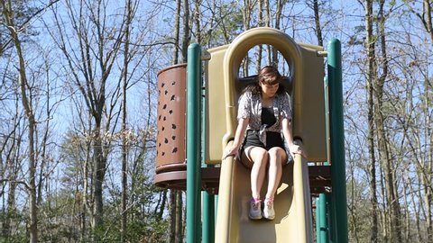 Front of young adult woman walking, sliding, playing slide on children playground outside, outdoors, park