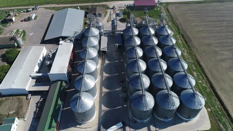 Aerial view. Large modern grain complex among the vast southern fields. Storage of cereal crops in huge gray metal tanks on a modern current. Agricultural scenery with silos at low altitude.