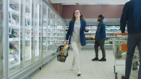 At the Supermarket: Happy Young Girl Holding Shopping Basket Dances Through Frozen Goods and Dairy Products Section of the Store. Shot on RED EPIC-W 8K Helium Cinema Camera.