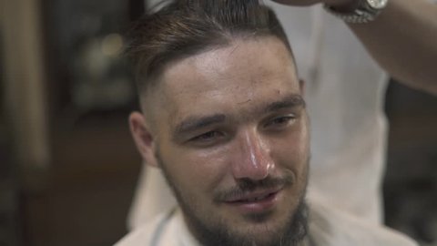 Face young man getting stylish hairdo in barbershop. Haircutter combing hair and cutting hair with hairdressing scissors in male salon. Close up hand hairdresser cutting wet male hair