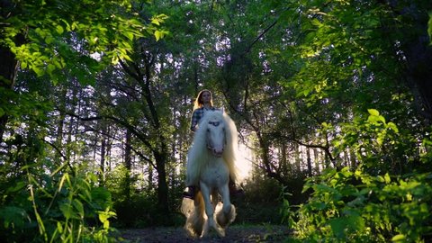 A young girl is riding on a beautiful white horse in the forest.