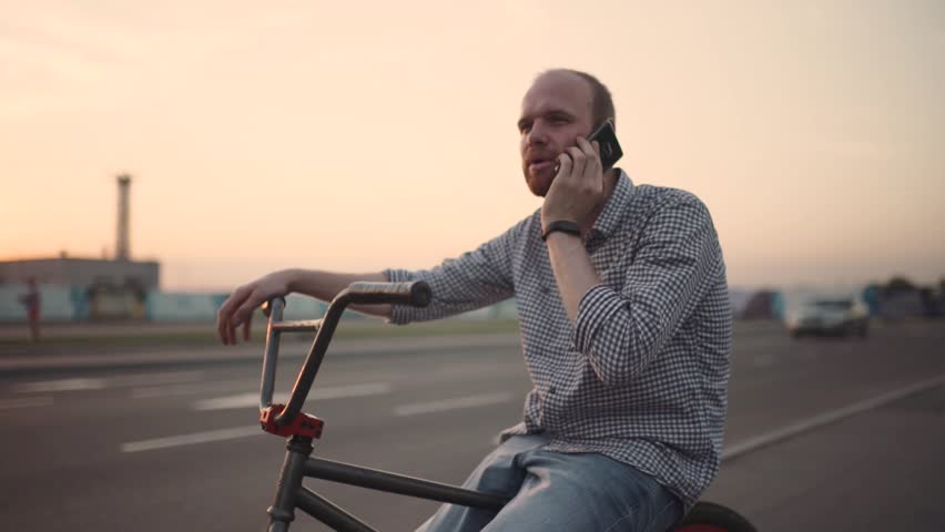 Young man with bmx bicycle uses his phone at sunset on the street. Slow motion