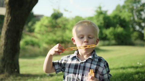 Little boy blowing soap bubbles in summer park Slow motion Full HD