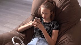 Young girl sitting in an armchair using a mobile phone engrossed in browsing or reading a text message in a slow rotating zoom in
