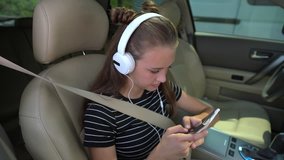Camera zooming out from girl with white headphones tapping phone screen while sitting in passenger seat of car
