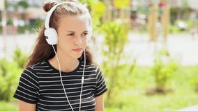 Slow motion of a young teenager listening to music as she walks along outdoors in the sunshine in a close up view