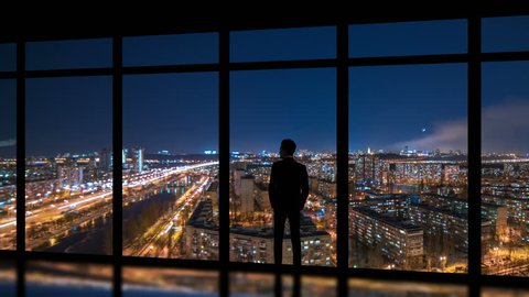 The man standing near windows on a night metropolis background. time lapse