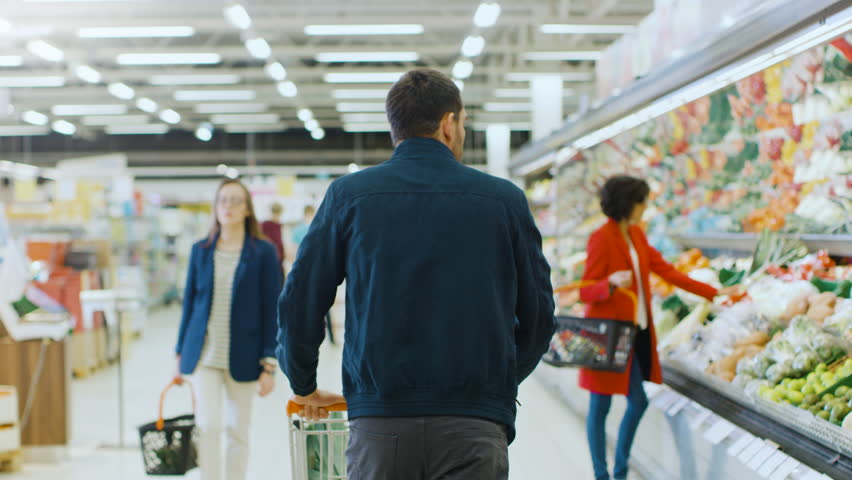At the Supermarket: Man Pushing Shopping Cart Through Fresh Produce Section of the Store. Store with Many Customers Shopping. Following Back View Shot. Shot on RED EPIC-W 8K Helium Cinema Camera. Royalty-Free Stock Footage #1015805119