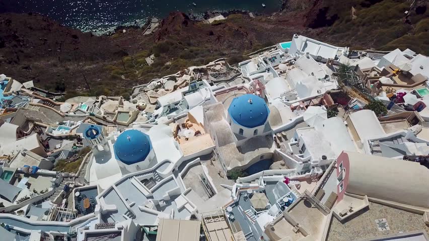 Aerial drone view looking down on beautiful white houses and church with blue dome rooftops in Santorini Greece