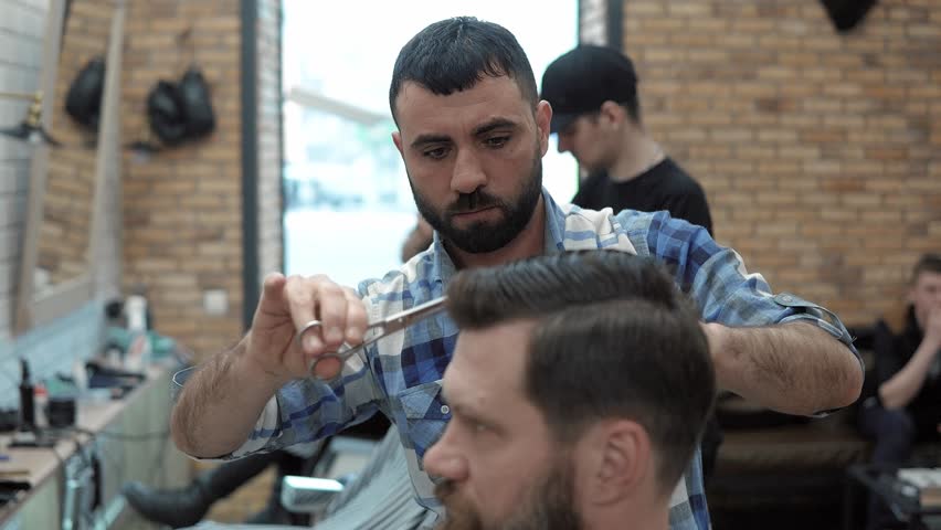 Close-up of barber cuts the hair by scissors at barbershop. Hairdresser's hands at working process. Barber making haircut of attractive bearded man in barbershop. Hairdresser at work. Beauty saloon. | Shutterstock HD Video #1015820491