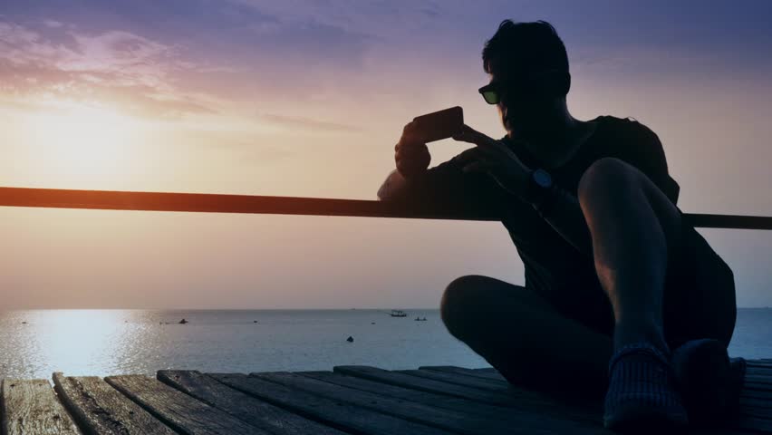 Guy sits on the dock and looks into the smartphone in timelapse