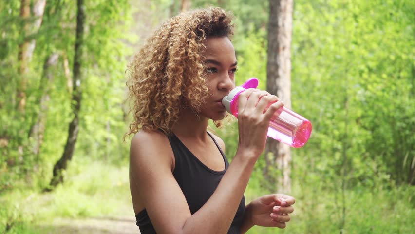 Black woman drinking from pink bottle. Portrait of black young woman taking break while jogging Royalty-Free Stock Footage #1015830175